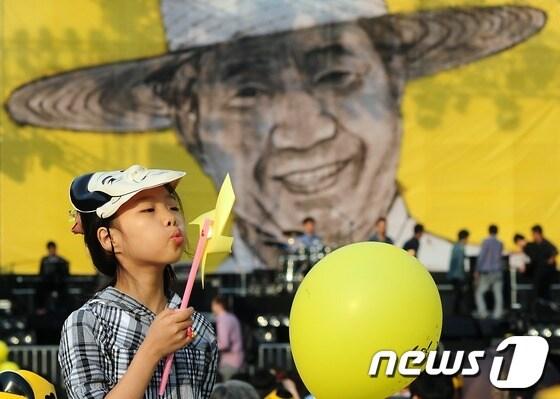 본문 이미지 - 노무현 전 대통령 서거 3주기를 앞두고 추모콘서트가 열린 19일 서울광장을 찾은 한 아이가 '노무현 가면'을 쓰고 노란 바람개비를 불고 있다.  2012.5.19/뉴스1 © News1 한재호 기자