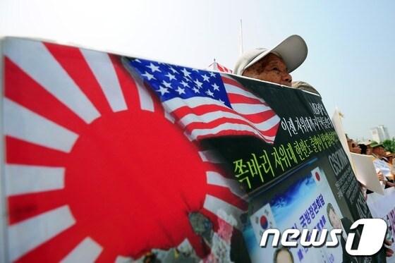 본문 이미지 - 김관진 국방장관이 이르면 6월 중 일본을 방문해 한일간 군사협력에 관한 협정을 체결할 예정이라고 알려져 논란이 되고 있는 9일 오전 서울 용산 국방부 앞에서 평통사, 민주노총, 정대협을 비롯한 시민단체 주최로 열린 '동북아 신냉전 불러올 한일 군사협정 체결 반대' 기자회견에서 한 참가자가 일본의 욱일승천기와 성조기가 그려진 규탄 팻말을 들고 있다. 한일 양국의 정식 군사협정 체결은 1945년 우리나라가 일제 식민지에서 해방된 이후 처음이다. 2012.5.9/뉴스1 © News1 한재호 기자