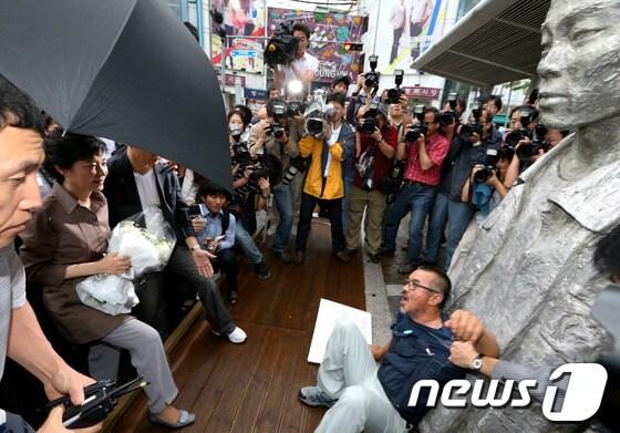 본문 이미지 - 박근혜 새누리당 대선 후보가 28일 오전 서울 종로구 창신동 전태일재단 방문이 가로막히자 청계천 전태열 열사 동상으로 발길을 옮겼으나 쌍용차지부장 김정우 씨가 동상 앞에 누워 헌화를 막고 있다. 박 후보 측은 이번 방문을 