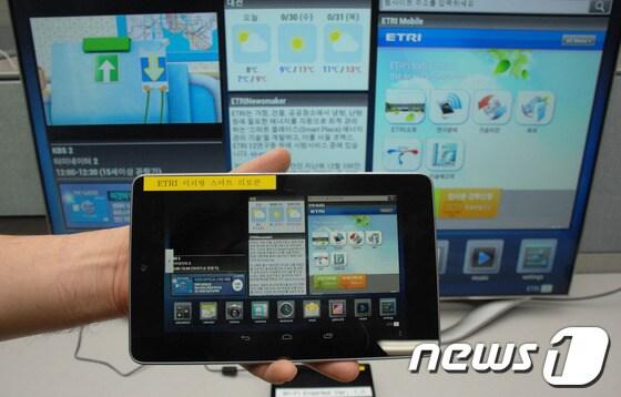 본문 이미지 - ETRI연구원이 이번에 개발된 스마트TV 미러형 리모콘을 시연해보이고 있다. 뒤쪽의 화면과 인터페이스가 동일하다.© News1 
