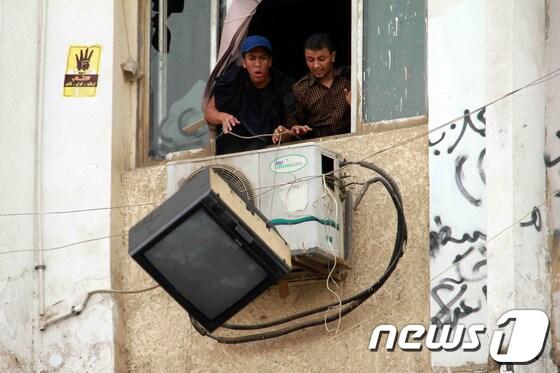 본문 이미지 - 30일(현지시간) 이집트 카이로의 알 아즈하르 대학 학생들이 反군부 시위를 벌이면서 빌딩 창문에서 TV를 던지고 있다. 이집트 보안군은 축출된 모하메드 무르시 전  대통령 지지 시위를 벌이는 학생들을 해산시키기 위해 최루탄을 쐈다. © AFP=뉴스1  