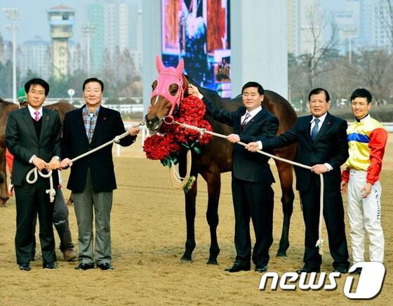 본문 이미지 - 8일 과천 서울경마공원에서 열린 서울사회복지공동모금회 연말나눔 캠페인에서 경주마 `지금이순간'이 사랑의 열매를 받은 뒤 최성룡(왼쪽 둘째) 마주와 지용철(〃 셋째)감독,  문세영(〃 첫째)선수 등과 기념사진을 찍고 있다./사진제공=한국마사회© News1