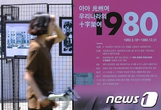 본문 이미지 - 5.18 민주화운동 33주년을 이틀 앞둔 16일 오후 서울 시청 앞 서울광장에서 한 시민이  전시중인 5.18 기록사진 앞을 지나고 있다. /뉴스1 © News1 박철중 기자