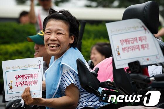 본문 이미지 - 광화문광장 해치마당 지하도 노숙농성 300일을 맞아 서울 종로구 계동 보건복지부 앞에서 열린 장애등급제·부양의무제 폐지 촉구 집회에 참석한 한 장애인이 밝은 표정으로 손팻말을 들고 있다. © News1 유승관 기자