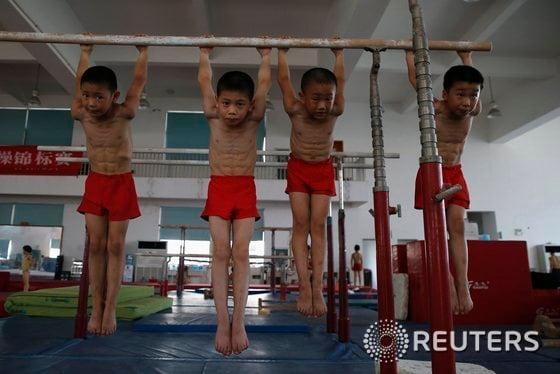 본문 이미지 - 14일 중국 저장성 자싱의 한 체육학교 체육관에서 어린 체조선수들이 나무봉에 매달려 스트레칭을 하고 있다. 이 학급은 6~8세로 구성돼 있는데 적어도 3년 동안 전문 스포츠교육을 받는다. 이들의 일과는 오전에 일반 학업, 오후엔 운동이다. © 로이터=뉴스1 