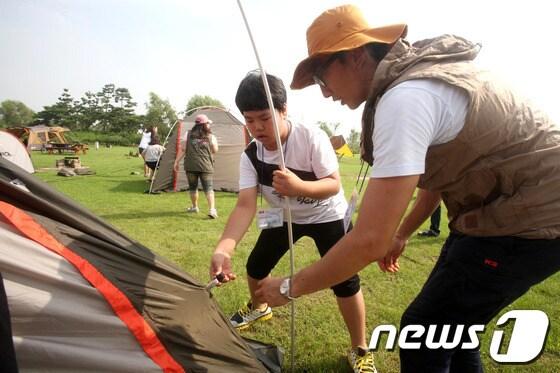 본문 이미지 - 지난해 7월 25일 노을캠핑장에서 진행된 가양4종합사회복지관의 1박 2일 K2 스쿨핑에 참여한 학생이 K2 오렌지 재능기부단의 시범에 따라 텐트치기에 도전하고 있다. /뉴스1 © News1 