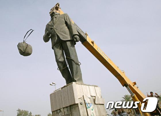 본문 이미지 - 2003년 이라크 바그다드에서 한 시민이 기중기로 사담 후세인 전 이라크 대통령 동상의 머리를 제거하고 있다. ⓒ AFP=뉴스1