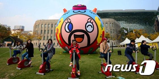 본문 이미지 - 6일 오후 서울광장에서 열린 높이 8m 돼지 형상 공공미술 '미스터 기부로' 설치 퍼포먼스에 참여한 시민 아티스트들이 자전거로 공기를 주입하고 있다.  ⓒ News1 박정호 기자