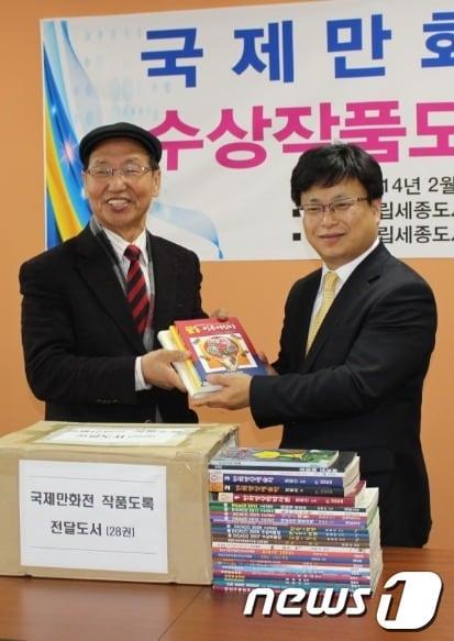 본문 이미지 - 임청산 국제만화영상원장(왼쪽)이 18일 세계10대 도서관에 22년간 개최해온 국제만화영상전 수상작품도록 전집 등을 기증했다.© News1 