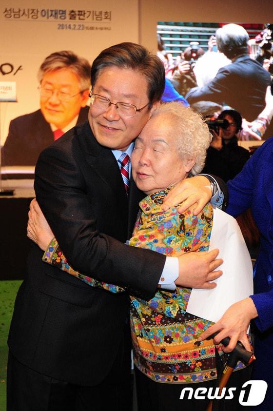 본문 이미지 - 2014년 2월 23ㅇ리 당시 이재명 성남시장이 경기 성남시 수정구 동서울대학교 국제교류센터에서 열린 자신의 저서 ‘오직 민주주의, 꼬리를 잡아 몸통을 흔들다’ 출판기념회에서 어머니를 소개하며 포옹하고 있다. ⓒ News1