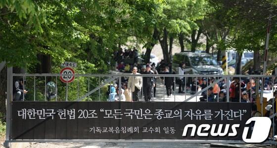 본문 이미지 - 14일 오전 기독교복음침례회의 총본산인 경기도 안성시 보개면 금수원에 종교의 자유를 주장하는 플랜카드가 걸려 있고 그 뒤로 신도들이 검찰의 체포영장 집행에 대비해 정문을 지키고 있다. 2014.5.14/뉴스1 © News1   손형주 기자