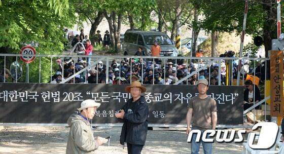 본문 이미지 - 14일 오전 기독교복음침례회의 총본산인 경기도 안성시 보개면 금수원에 종교의 자유를 주장하는 플랜카드가 걸려 있고 그 뒤로 신도들이 검찰의 체포영장 집행에 대비해 정문을 지키며 찬송가를 부르고 있다.기독교 복음침례회 측은 