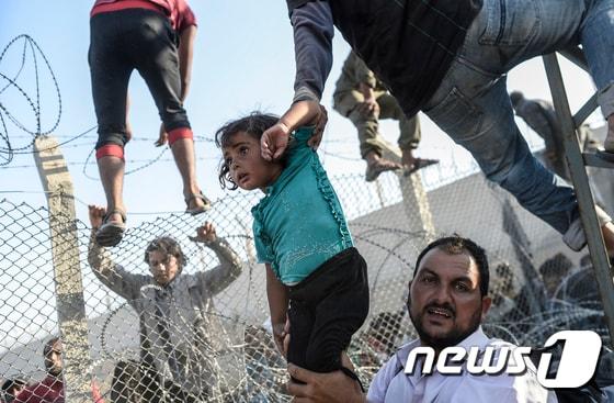 본문 이미지 - 전쟁을 피해 도망온 시리아 난민이 6월 14일 터키 동남부 접경지역인 샨리우르파 주 아차칼레 인근에서 터키 영토로 들어가기 위해 자신의 아이를 국경장벽 위로 들어 올리고 있다. ⓒ AFP=뉴스1