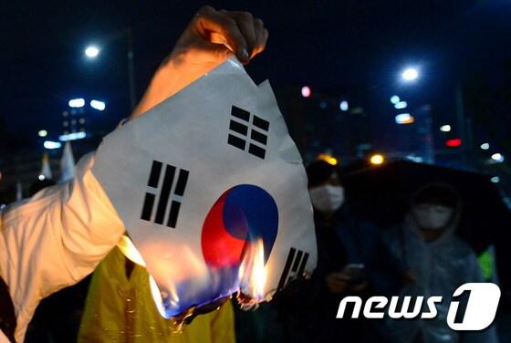 본문 이미지 - 세월호 참사 1년 전국 집중 범국민대회 참가자가 2015년4월18일 오후 서울 광화문 앞에서 경찰과 대치하는 도중 태극기를 불태우고 있다. 2015.4.18/뉴스1 ⓒ News1 박정호 기자