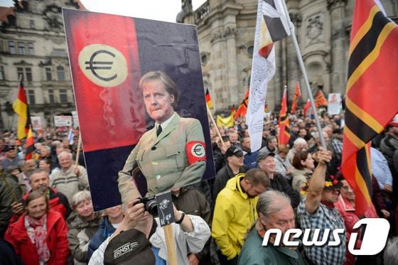 본문 이미지 - 독일의 반 이슬람 극우단체 '유럽의 이슬람화에 반대하는 애국적 유럽인들'(PEGIDA·페기다)가 지난해 6월 동부 드레스덴에서 나치 제복을 입은 앙겔라 메르켈 독일 총리의 합성 사진을 들고 시위를 하고 있다. ⓒ AFP=뉴스1