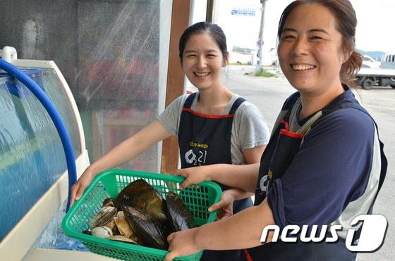 본문 이미지 - 장미선(왼쪽) 장혜선 자매가 주문이 접수된 조개를 수조에서 꺼내 들여보이고 있다. 두 자매는 도시생활을 접고 고향으로 돌아와 온라인 수산물  쇼핑몰을 창업해 제 2의 인생을 살아가고 있다. ⓒ News1 박현석 기자