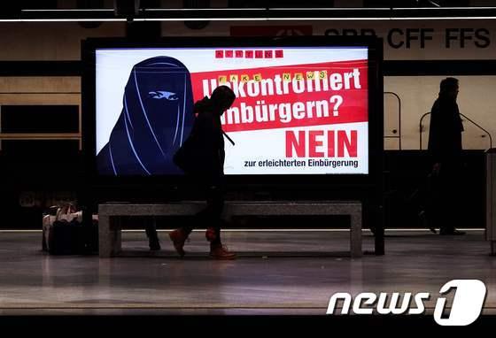 본문 이미지 - 지난 7일(현지시간) 검정색 니캅을 쓴 여성과 "통제되지 않는 귀화?"(Unkontrolliert einburgern)라는 글귀가 적힌 광고가 스위스 취리히의 길거리에 걸려 있다. ⓒ AFP=뉴스1