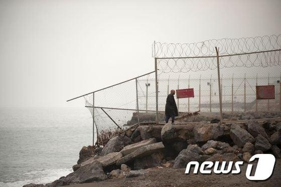 본문 이미지 - 한 남성이 모로코와 스페인령 세우타 국경에 설치된 철조망 옆을 지나치고 있다.  ⓒ AFP=뉴스1
