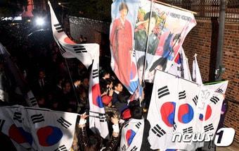 본문 이미지 - 박근혜 전 대통령이 헌법재판소의 탄핵심판 인용으로 청와대를 떠난 12일 저녁 서울 강남구 삼성동 사저로 들어가기는 도중 지지자들이 태극기로 박 전 대통령을 가리고 있다. 2017.3.12/뉴스1 ⓒ News1 이재명 기자