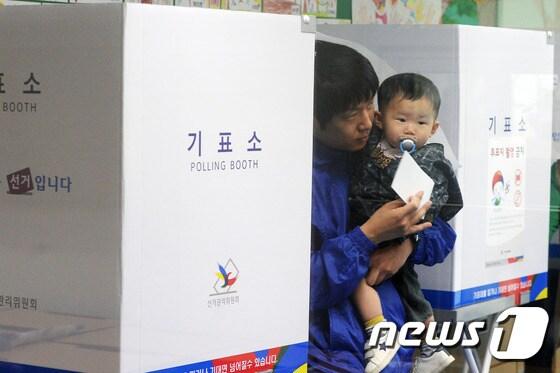 본문 이미지 - 제19대 대통령선거 투표일인 9일 경기 고양시 신원초등학교에 마련된 투표소에서 아이를 안은 유권자가 투표하고 있다. 2017.5.9/뉴스1 ⓒ News1 황기선 기자