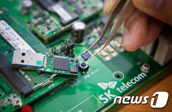 본문 이미지 - SK텔레콤 분당사옥에 위치한 ‘양자암호통신 국가시험망’에서 SK텔레콤 직원이 5x5mm 크기의 양자난수생성 칩을 들고 있는 모습. (사진제공=SKT)ⓒ News1