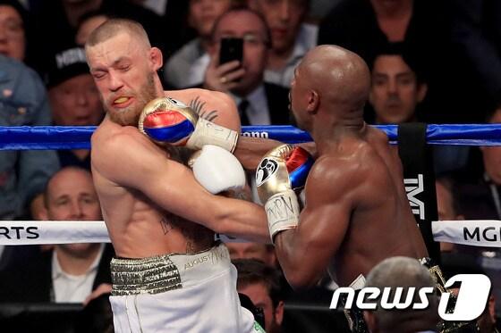본문 이미지 - 코너 맥그리거(왼쪽)가 27일 열린 플로이드 메이웨더와의 경기에서 펀치를 허용하고 있다. ⓒ AFP=News1