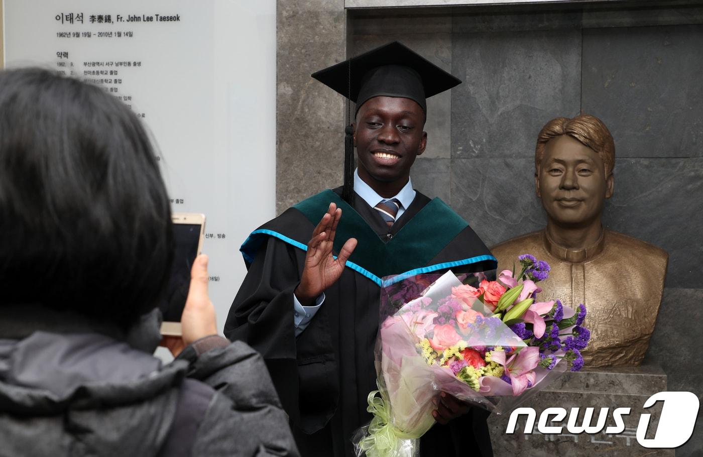 고 이태석 신부의 추천으로 남수단 톤즈에서 한국으로 유학 온 토마스 타반 아콧씨가 15일 오후 부산 인제대학교 부산캠퍼스 의과대학 졸업식에서 고 이태석 신부 흉상과 기념촬영을 하고 있다.2018.1.15/뉴스1 ⓒ News1 여주연 기자