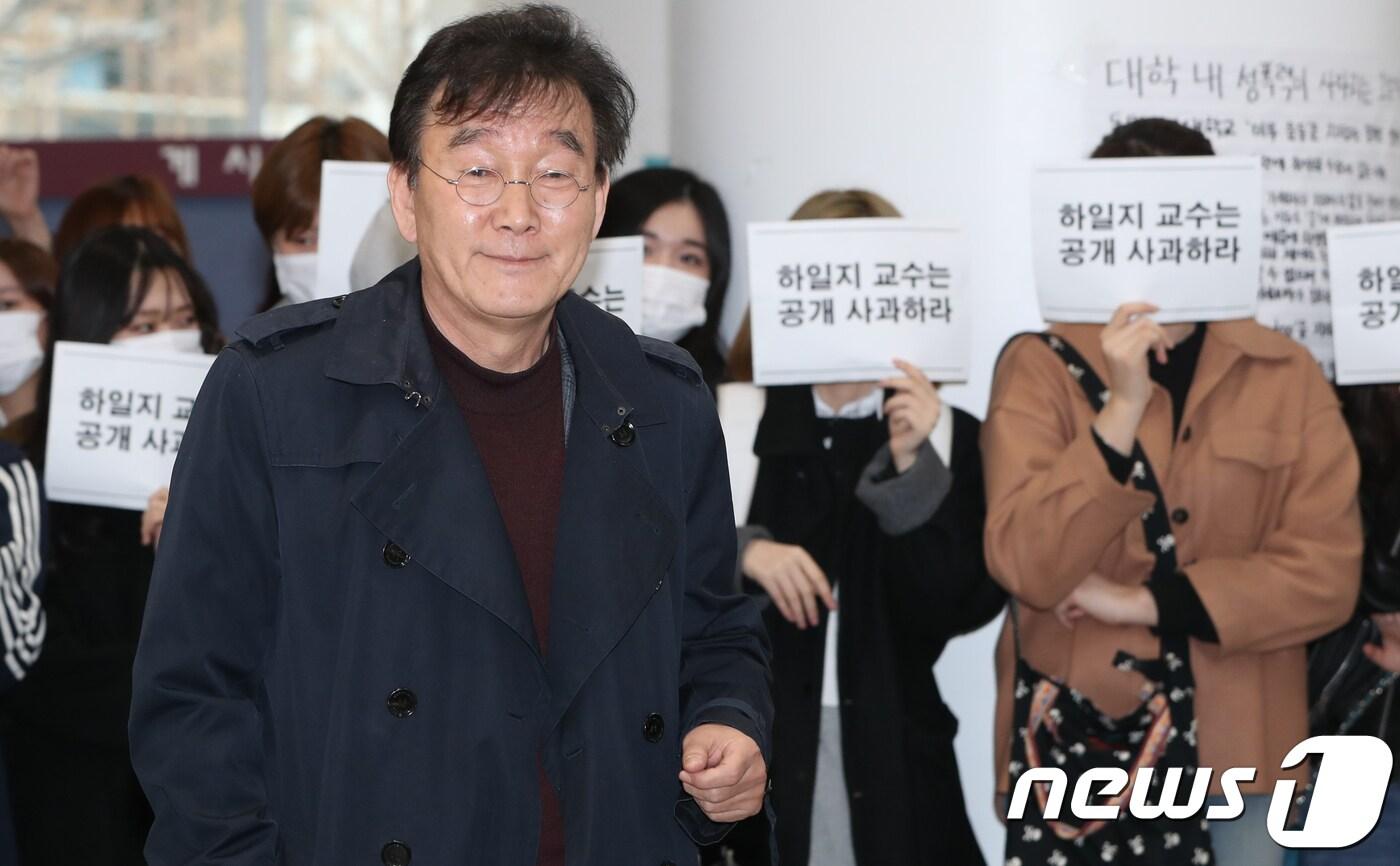 본문 이미지 - 하일지 동덕여대 문예창작과 교수가 19일 서울 성북구 동덕여대 백주년기념관에서 열린 ‘미투’ 비하 관련 해명 기자회견을 하기 위해 입장하고 있다. 뒤로는 재학생들이 손피켓을 들고 사과를 촉구하고 있다. 2018.3.19/뉴스1 ⓒ News1 허경 기자