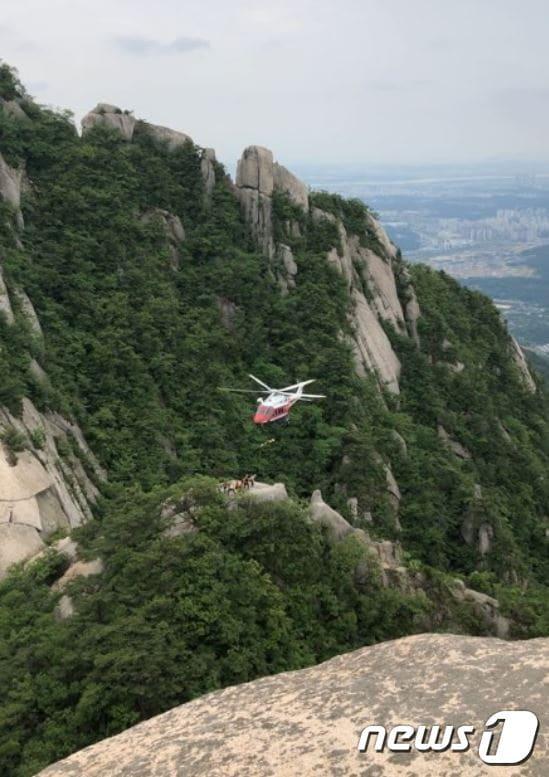 본문 이미지 -  소방구조헬기가 북한산 인수봉에서 암벽등반하던 중 자기확보줄을 걸어두지 않고 쉬다가 추락한 80세 여성을 구조해 옮기고 있다. ⓒ News1