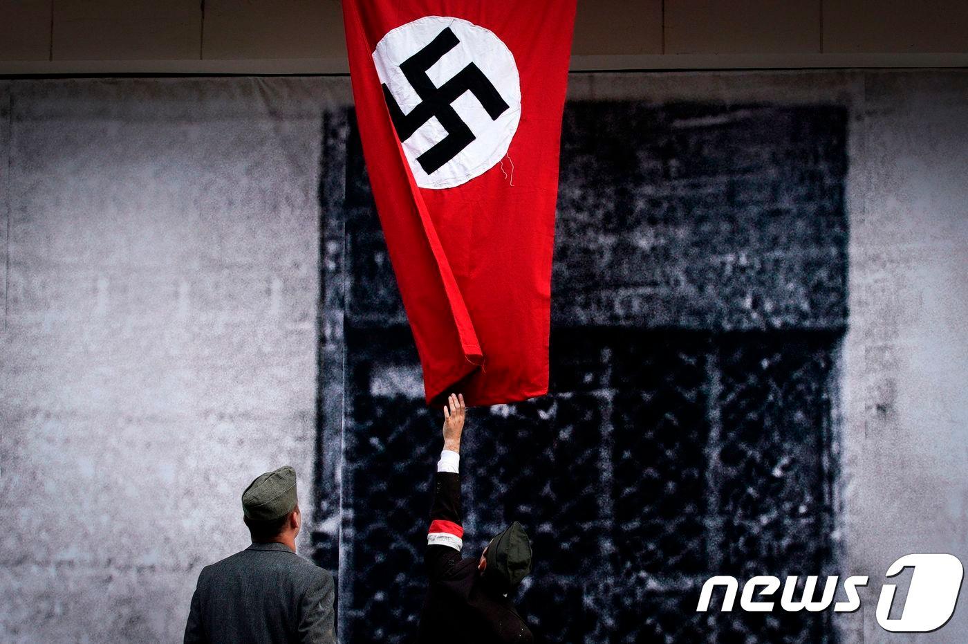 본문 이미지 - 폴란트 레지스탕스 복장을 한 공연가가 8월3일(현지시간) 폴란드 수도 바르샤바에서 제2차 세계대전 75주년을 기념해 공연하고 있다. 사진 속 깃발은 독일 나치즘의 상징 하켄크로이츠. ⓒ AFP=뉴스1