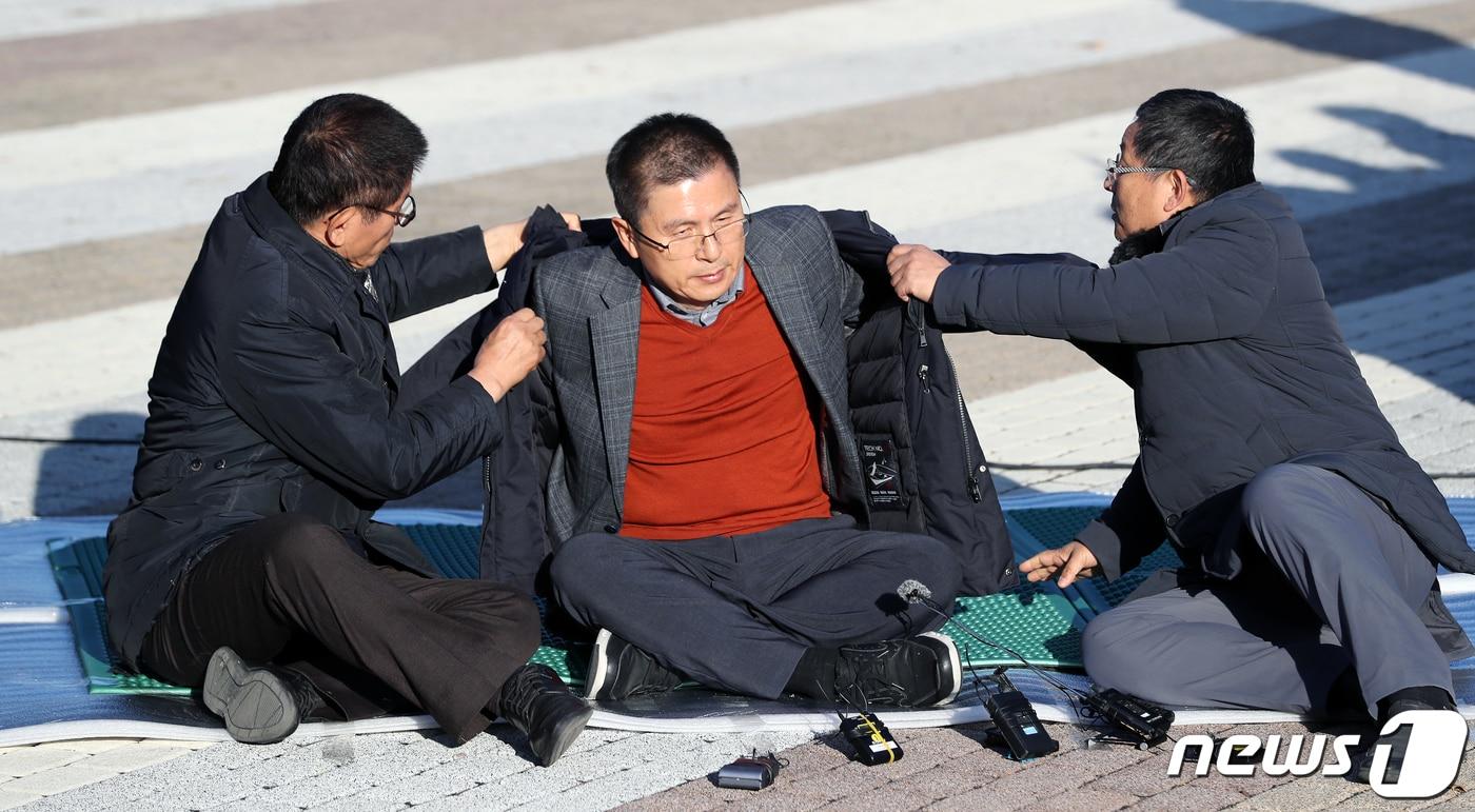 황교안 자유한국당 대표가 20일 오후 서울 종로구 청와대 사랑채 인근에서 지소미아 파기·패스트트랙 법안 강행 처리 등 철회, 문재인 정부의 실정에 따른 국정 대전환을 촉구하며 단식농성을 시작하고 있다. 김문수&#40;왼쪽&#41; 전 경기지사, 차명진 전 의원의 도움 받아 외투 입는 황교안 대표. 2019.11.20/뉴스1 ⓒ News1 이동해 기자