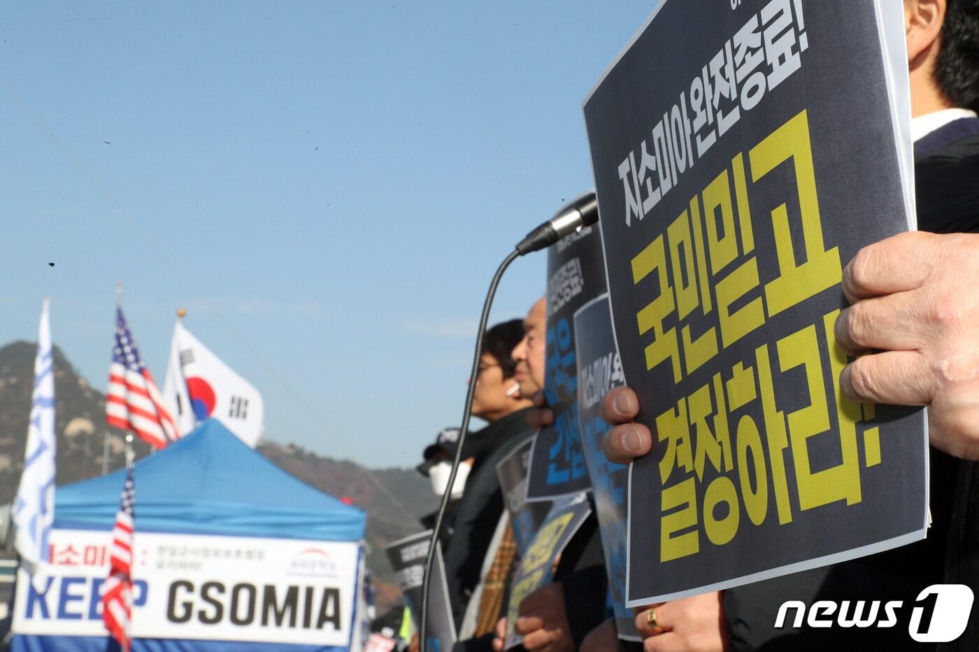 본문 이미지 - 아베규탄시민행동 회원들이 22일 오후 서울 광화문 광장에서 손팻말을 들고 한일 군사정보보호협정 (GSOMIA·지소미아) 폐기를 촉구하는 기자회견을 진행하고 있다. 뒷편으로 우리공화당이 설치한 지소미아 유지를 촉구하는 현수막이 걸려있다. 지소미아는 오는 22일 자정 종료를 앞두고 있다. 2019.11.22/뉴스1 ⓒ News1 황기선 기자