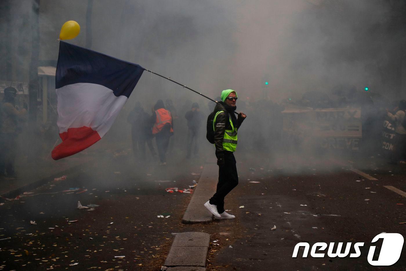 본문 이미지 - 5일(현지시간) 프랑스 파리에서 열린 연금개편 반대 시위에 참석한 시위대가 최루탄 연기가 자욱한 가운데 프랑스 국기를 들고 서 있다. ⓒ AFP=뉴스1