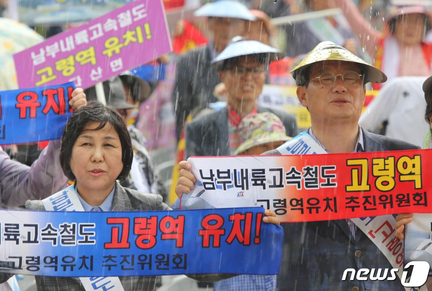 본문 이미지 - 14일 경북 고령군 문화누리 야외공연장에서 열린 '남부내륙고속철도 고령역 유치 범군민 결의대회'에서 곽용환 군수(오른쪽)와 배효임 고령군의회부의장(왼쪽)이 소나기가 내리는 가운데 군민들과 함께 '고령역 유치'가 적힌 손 피켓을 들고 구호를 외치고 있다. 소나기가 오는 와중에도 자리를 뜨지 않은 3000여명의 군민들은 취타대와 KTX모형을 앞세우고 축협네거리를 거쳐 중앙네거리까지 행진을 하며 최적의 경제성과 효율성을 가진 고령군에 남부내륙철도 역사설치를 요구했다.2019.5.14/뉴스1 ⓒ News1 정우용 기자