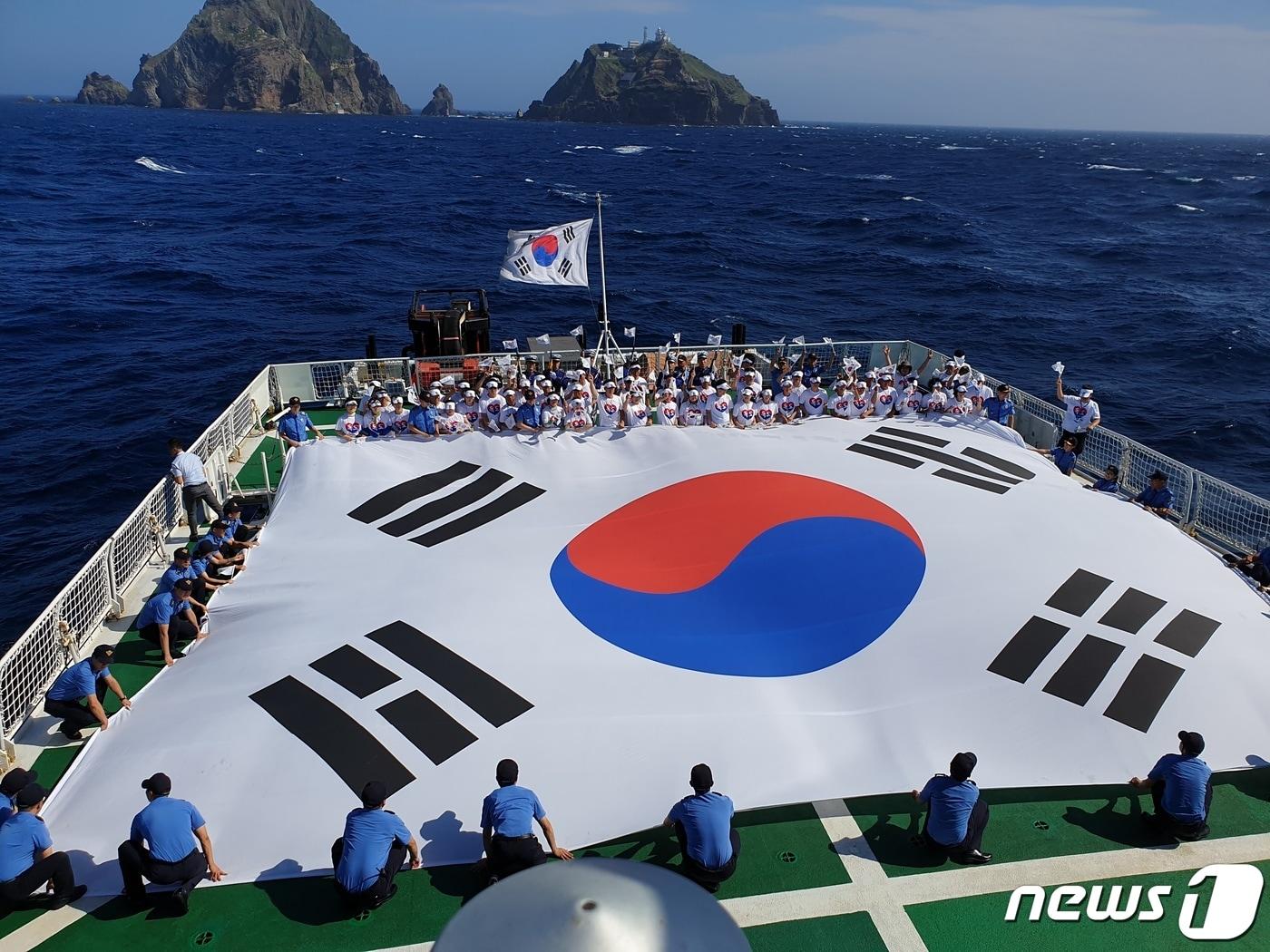 본문 이미지 - 74주년 광복절을 하루 앞둔 14일 해양경찰교육원 소속의 '바다로함'을 타고 독도 바다를 찾은 '독도 해양영토순례단'이 독도를 배경으로 대형 태극기를 펼쳐 기념 사진을 찍고 있다. 이번 행사는 순국선열의 숭고한 정신을 되새기고 해양영토 수호 의지를 다지기 위해 실시됐으며 독립유공자 가족, 정책자문위원, 일반국민 등 130여명이 함께했다.(해경교육원 제공)2019.8.15 /뉴스1 ⓒ News1 
