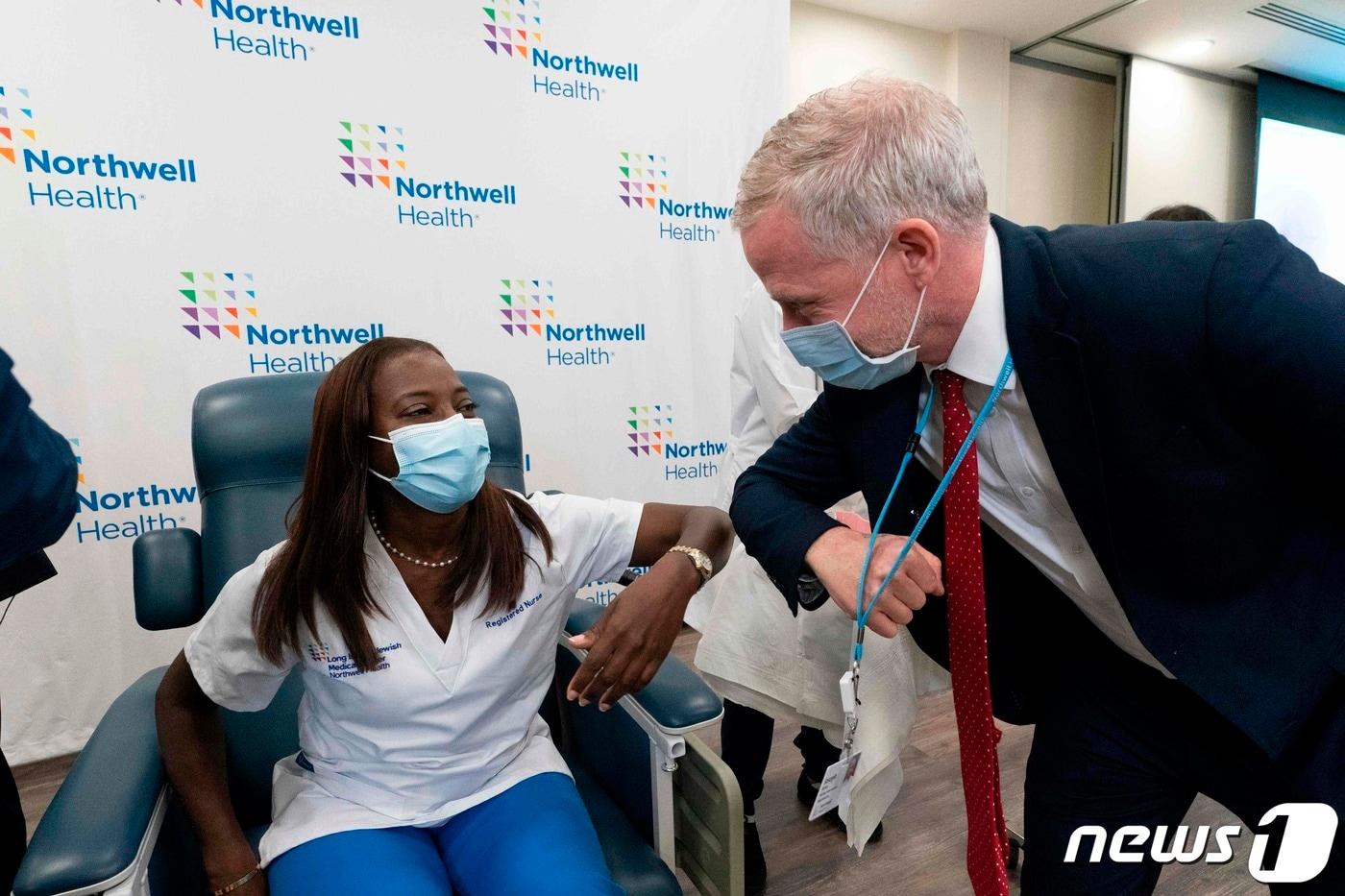 본문 이미지 - 14일(현지시간) 뉴욕 퀸스의 롱아일랜드 주이시 메디컬 센터에서 간호사 샌드라 린지가 미셸 체스터 의사로부터 화이자ㆍ바이오앤테크의 코로나19 백신을 미국서 처음으로 접종받은 뒤 병원 홍보 담당자와 팔꿈치를 맞대고 있다. ⓒ AFP=뉴스1 ⓒ News1 우동명 기자