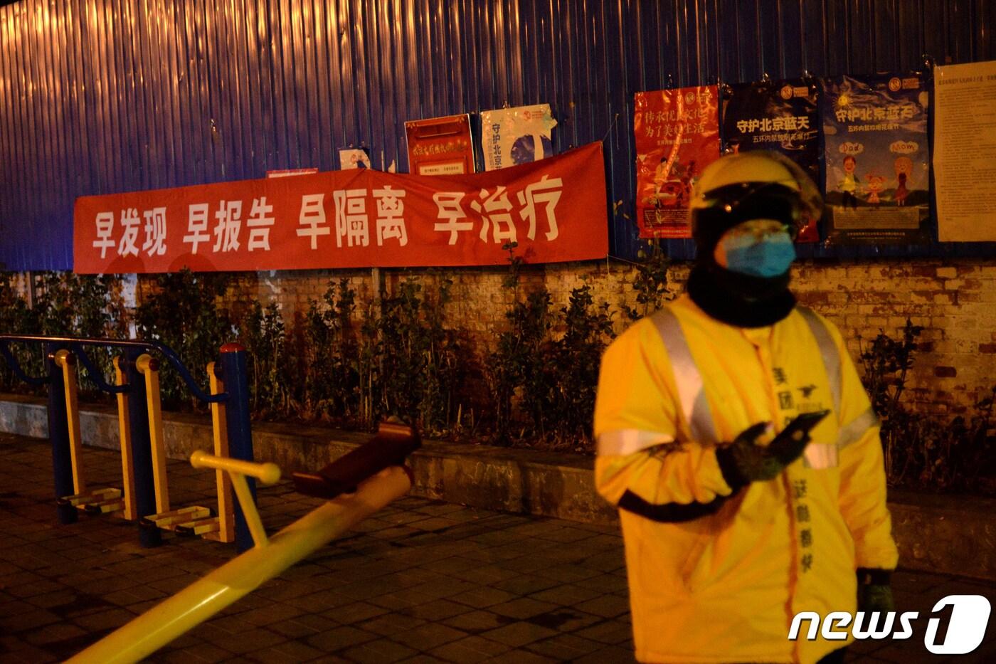 베이징의 한 주택가 옆에 '일찍 발견하고 보고하자'는 현수막이 걸려있다. 현수막 옆에서 메이퇀 배달원이 음식을 배달하기 위해 기다리고 있다. ⓒ 로이터=뉴스1 ⓒ News1 윤다혜 기자