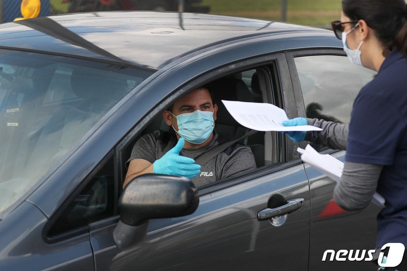 본문 이미지 - 8일(현지시간) 코로나19 확산 속 플로리다주 하이얼리어의 존 F. 케네디 도서관 앞 도로에서 시민이 실업수당 신청서를 받고 있다. ⓒ AFP=뉴스1