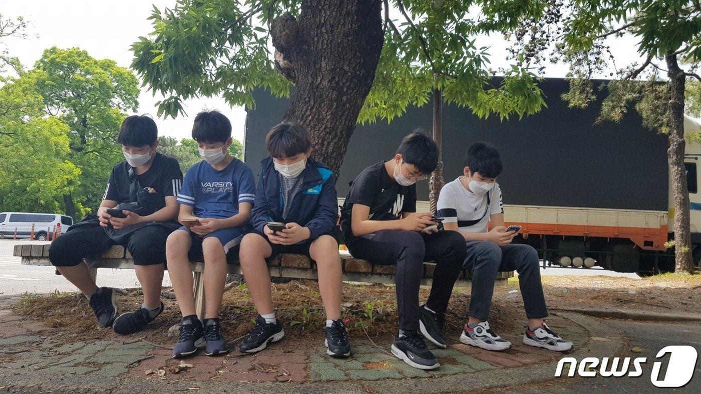 본문 이미지 - 24일 오후 경북 경주시 황성공원 내 시립도서관을 찾은 초등학생들이 친구들과 함께 나무 그늘 밑에 앉아서 스마트 폰을 하고 있다.  ⓒ 뉴스1 최창호 기자