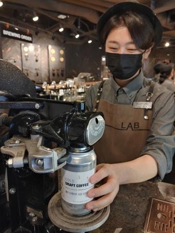 본문 이미지 - 이디야커피 본사 직영 커피랩 매장에서 직원이 캔 실링기를 이용해 커피를 포장하고 있다.(이디야커피 제공) 