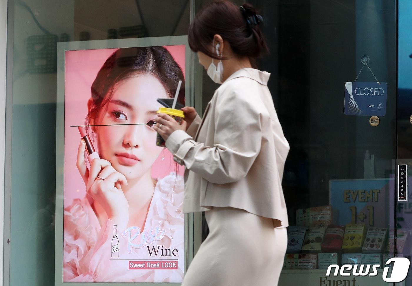 서울 명동의 문 닫은 화장품 가게 앞을 한 시민이 답답함에 마스크를 턱에 걸쳐둔 채 지나가고 있다./뉴스1 ⓒ News1 이동해 기자