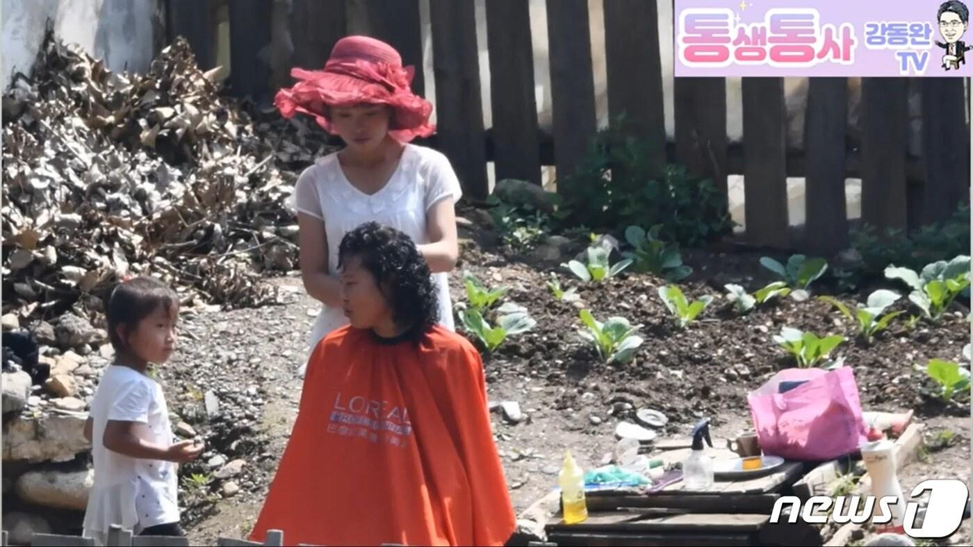 본문 이미지 - 북한의 양강도 삼수군 지역 주민들이 마을 창고 뒤편에서 출장 미용 서비스를 받고 있다. ('통생통사 강동완 TV' 갈무리) ⓒ 뉴스1