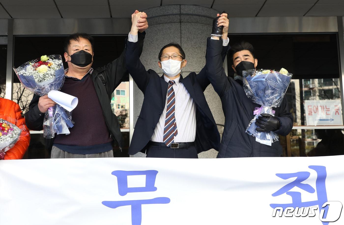 본문 이미지 - ‘낙동강변 살인사건’ 범인으로 지목돼 21년간 옥살이를 한 장동익씨와 최인철씨가 2021년 12월 4일 부산 연제구 부산고등법원에서 열린 재심 선고 공판을 박준영 변호사(가운데)와 손을 들어보이고 있다. ⓒ News1 여주연 기자