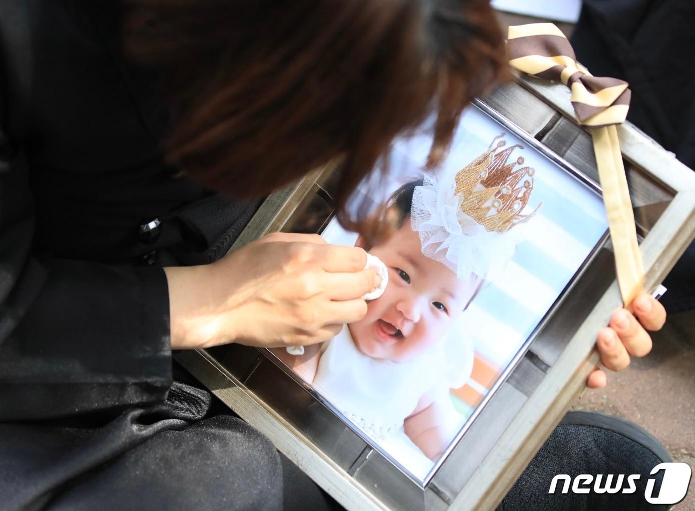 본문 이미지 - 16개월 된 입양아 정인양을 학대해 숨지게 한 혐의를 받는 양부모의 1심 선고공판이 열린 지난 2021년 5월 14일 오후 양천구 서울남부지방법원 앞에서 상복을 입은 한 시민이 정인이 사진을 닦고 있다. 2021.5.14/뉴스1 ⓒ News1 구윤성 기자