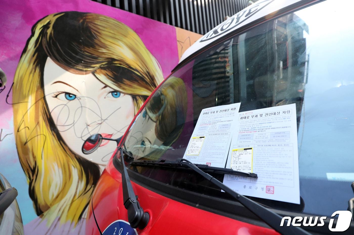 30일 오전 서울 종로구의 한 서점 벽면에 그려진 윤석열 전 검찰총장의 배우자 김건희 씨를 비방하는 내용의 벽화를 가린 보수단체 차량에 주차위반 과태료 통지서가 붙어 있다. 2021.7.30/뉴스1 ⓒ News1 황기선 기자