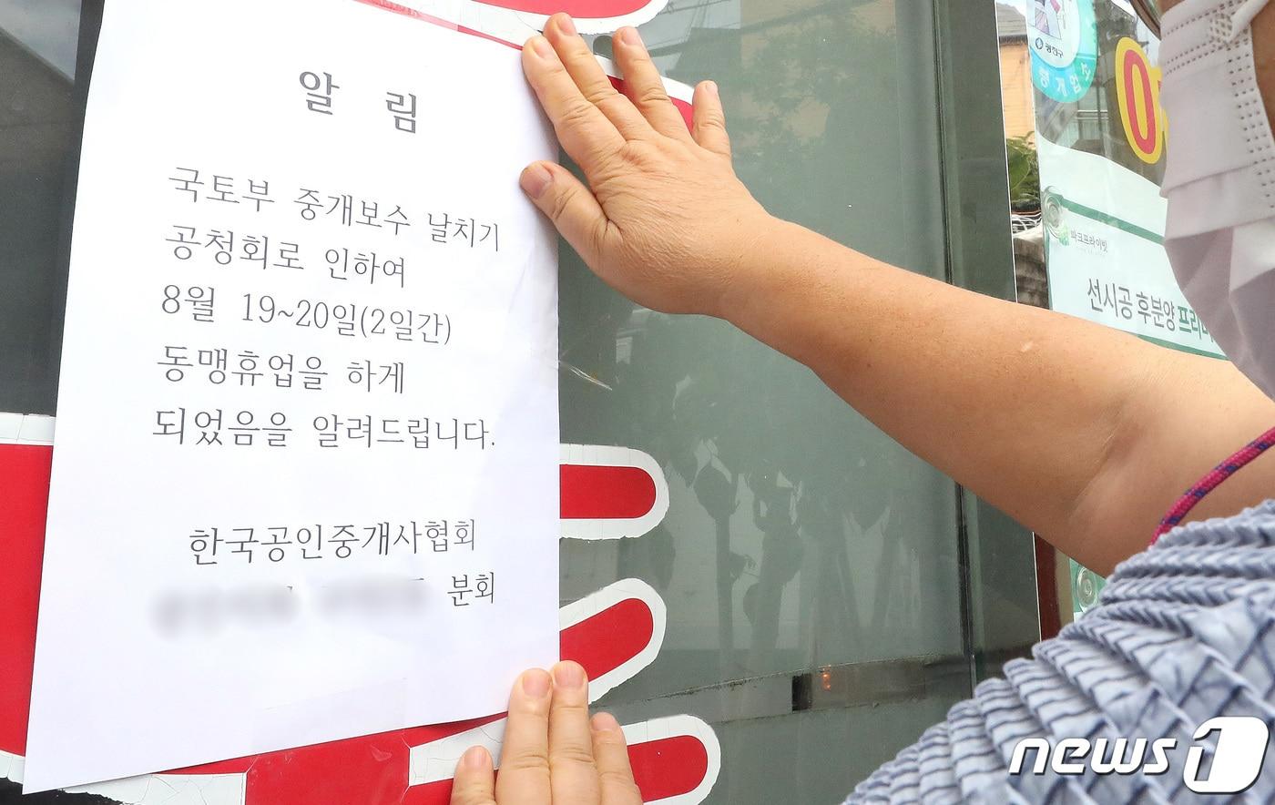 19일 오후 서울 시내의 한 부동산에서 관계자가 국토교통부의 중개보수 날치기 공청회로 인한 동맹휴업을 알리는 안내문을 붙이고 있다. 2021.8.19/뉴스1 ⓒ News1 임세영 기자