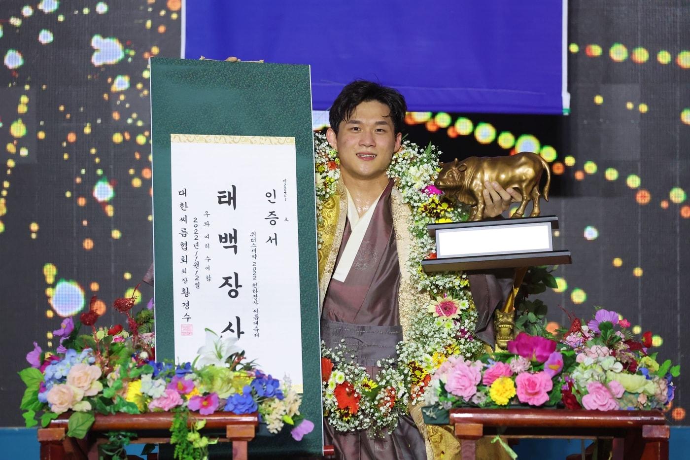 본문 이미지 - 12일(토) 울산광역시 울주군 작천정운동장 씨름특설경기장에서 열린 ‘위더스제약 2022 천하장사씨름대축제’ 태백장사(80kg이하)에 등극한 노범수(울주군청)가 장사꽃가마를 타고 장사인증서와 황소트로피를 들고 기념사진을 찍고 있다.(대한씨름협회 제공)