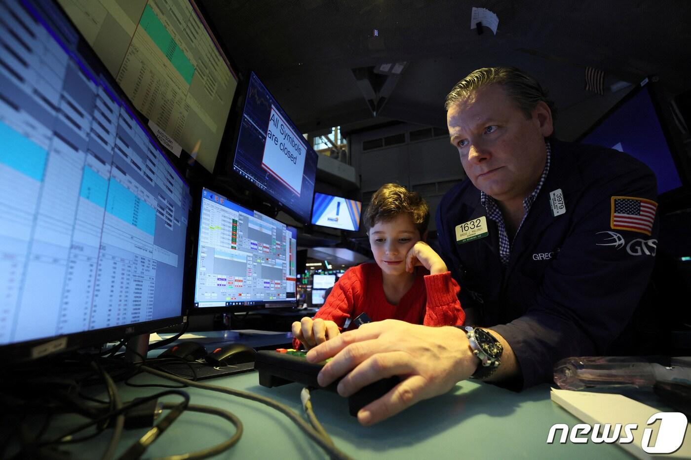 본문 이미지 - 뉴욕증권거래소(NYSE) 내부 객장의 한 트레이더가 추수감사절 다음날인 블랙프라이데이 자녀를 데리고 와서 구경시켜 주는 행사에 참여하며 컴퓨터 화면을 쳐다 보고 있다. 2022.11.25 ⓒ 로이터=뉴스1