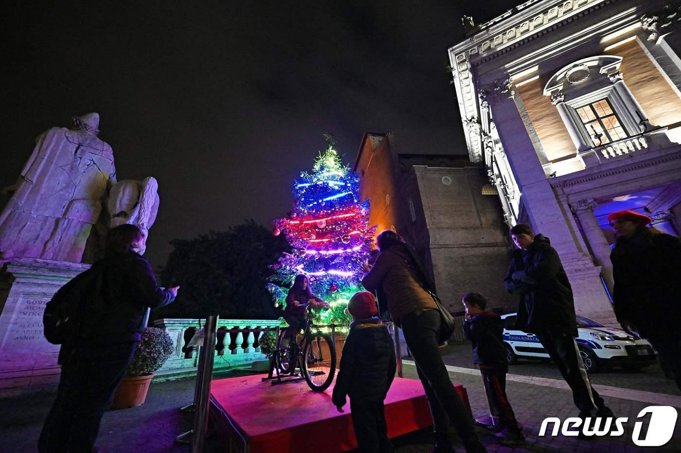 26일(현지시간) 이탈리아 로마에서 한 시민이 시청에서 설치한 성탄 트리에 불을 밝히기 위해 자전거 페달을 열심히 밟고 있다. 트리 인근에는 총 6개의 자전거가 설치돼 로마 관광객들의 수고를 자체 전력원으로 삼고 있다. 2022.12.26. ⓒ AFP=뉴스1 ⓒ News1 김성식 기자