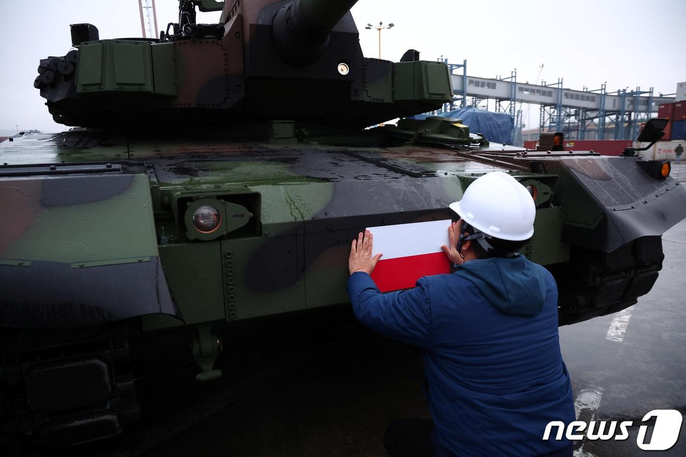 본문 이미지 - 2022년 12월 폴란드 그디니아 항구에 한국산 K2 전차와 K9자주포가 처음 입고됐다. 현장 노동자가 폴란드 국기가 그려진 스티커를 전차에 부착하고 있다. 2022.12.7. ⓒ 로이터=뉴스1 ⓒ News1 권진영 기자